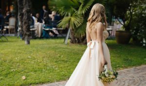 Braut mit Hochzeitskleid und offenen langen Haaren und Haarschmuck steht vor einer Wiese