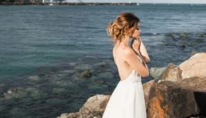 Junge Braut mit gesteckter Hochzeitsfrisur posiert für Foto an einer Klippe am Meer