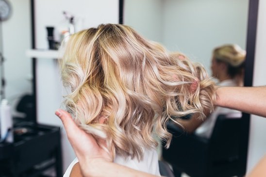 Frau mit blonden Haaren bekommt eine Haarverdichtung beim Friseur