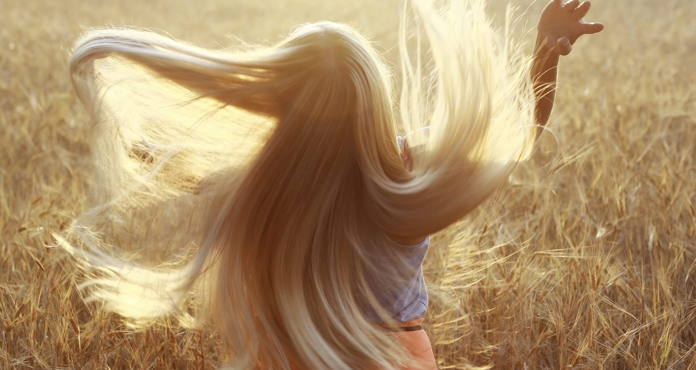 Fettige Haare: Frau mit blonden langen Haaren schwingt ihre Haare im Getreidefeld