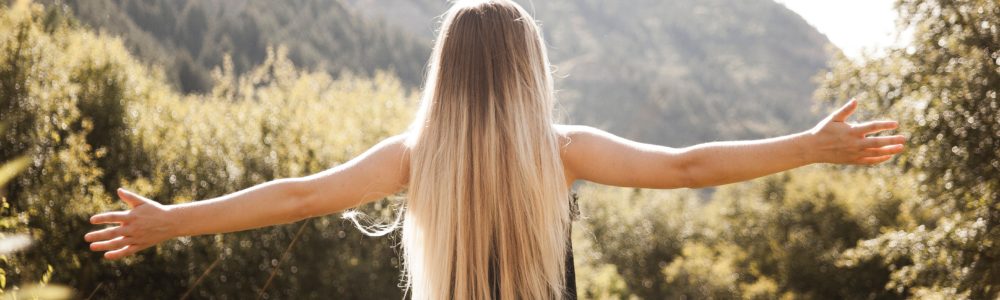 Junge Frau mit langen blonden feinen Haaren steht im auf einer Wiese