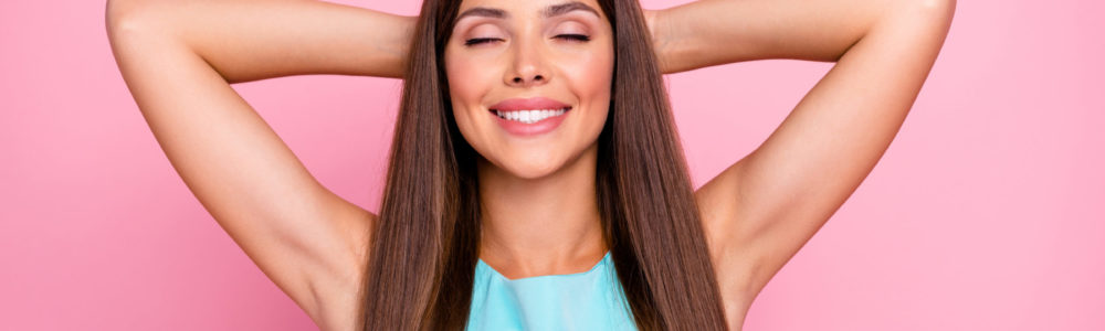 Junge lächelnde Frau posiert mit schönen langen brünetten Haaren vor einem pinken Hintergund