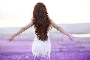 Frau mit schönen, langen Haaren genießt den Sonnenuntergang mit offenen Armen in Lavendelfeld